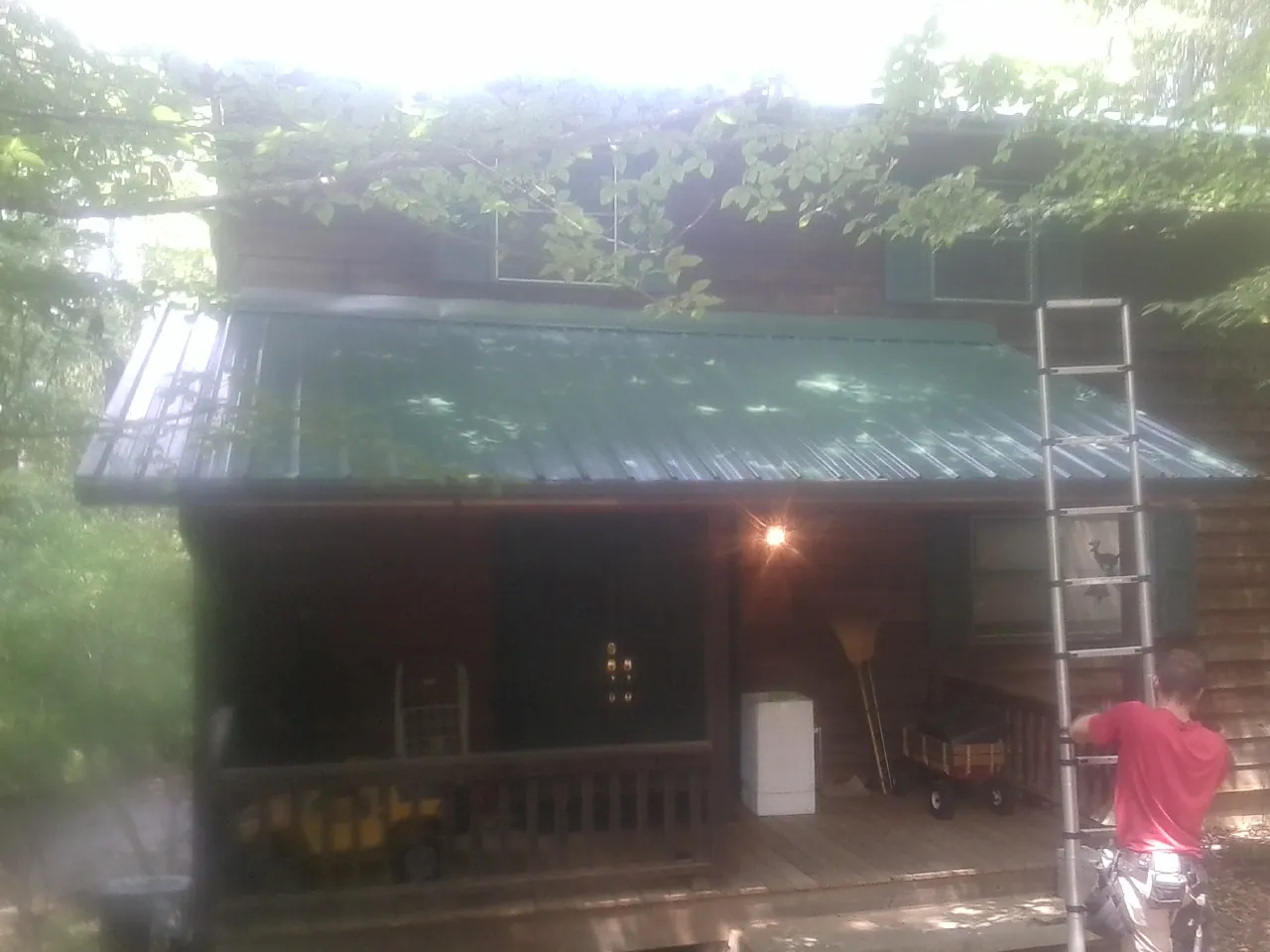 Worker on a ladder at the green porch roof of a wooded cabin in Stratford