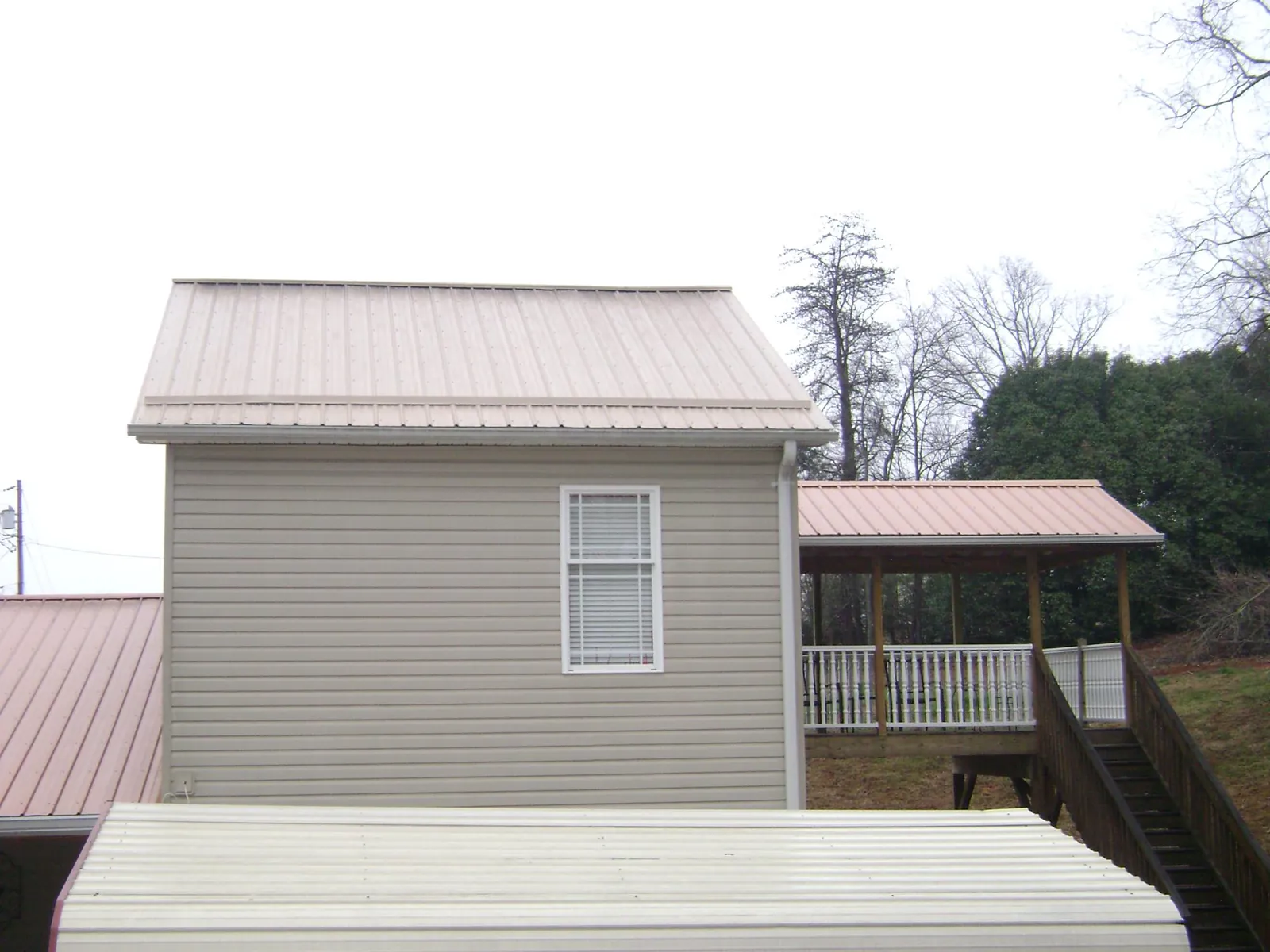 Tan metal roofs on a two story addition and attached porch, from a Roof Replacement job in Stratford